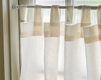 May include: White linen curtains with a beige band at the top, hanging from a white curtain rod. The curtains are semi-sheer, allowing light to filter through. The window is visible in the background.