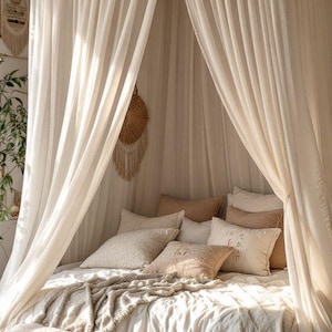 May include: A white sheer canopy draped over a bed with white bedding and several brown throw pillows. The bed is on a light brown rug.