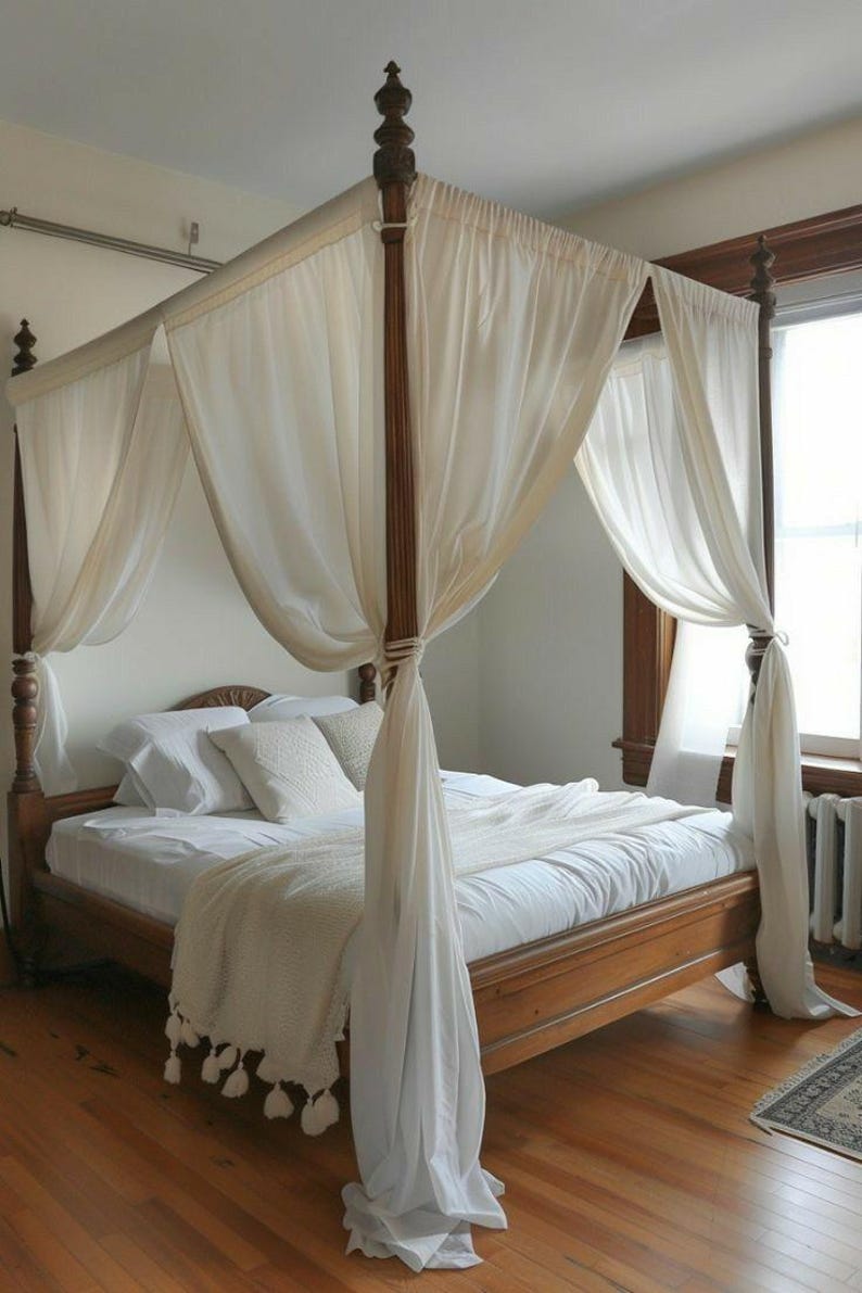 May include: A wooden four-poster bed with white sheer curtains draped over the top. The bed is made with white linens and a white throw blanket with tassels.