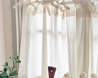 Puede incluir: Cortinas de lino color crema con detalles anudados en la parte superior, colgadas frente a una ventana. Las cortinas se combinan con una tabla de cortar de madera y flores blancas, creando una estética suave y natural. El marco de la ventana es blanco.