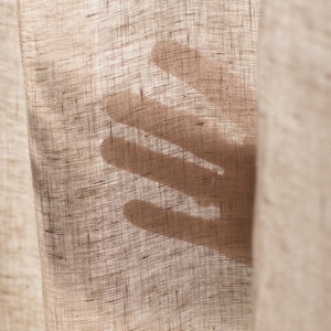May include: A close-up of a sheer, light brown linen curtain with a shadow of a hand cast on it.