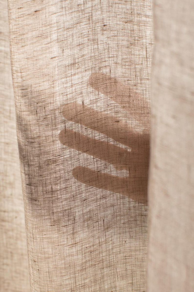 May include: A close-up of a sheer, light brown linen curtain with a shadow of a hand cast on it.
