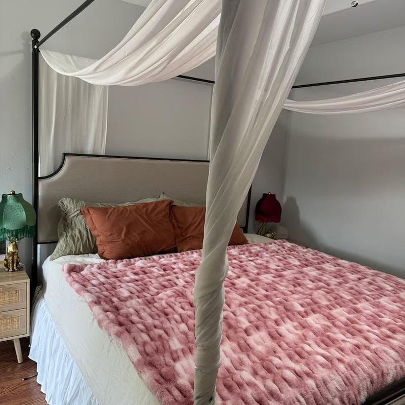 May include: A canopy bed with a white canopy and a pink and white patterned blanket. The bed has a headboard and footboard and is made of metal.