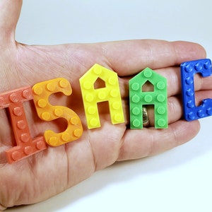 May include: The name "ISAAC" spelled out using colorful plastic letters that resemble Lego bricks. The letters are orange, yellow, green, and blue.