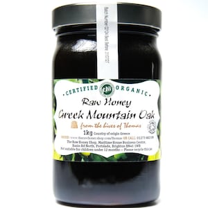 May include: A glass jar of raw honey from Greece. The label reads "Certified Organic Raw Honey Greek Mountain Oak from the hives of Thomas 1kg Country of origin Greece".