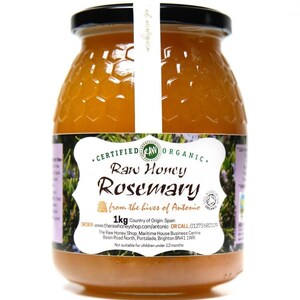 May include: A glass jar of raw rosemary honey, labeled "Certified Organic Raw Honey Rosemary from the hives of Antonio". The jar is 1 kg and has a white label with black text. The label also includes the company's website and phone number.