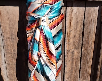 Peut inclure: Un bandana rayé turquoise, orange et blanc avec un fermoir en bois. Le bandana est noué autour d'un poteau en bois.