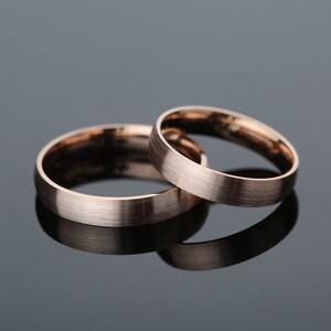 May include: Two rose gold wedding bands, one slightly wider than the other, with a brushed finish.