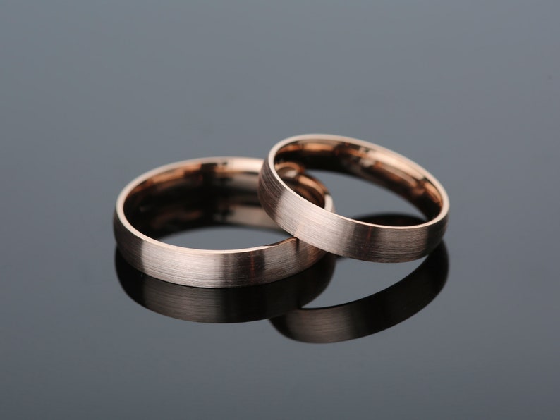 May include: Two rose gold wedding bands, one slightly wider than the other, with a brushed finish.