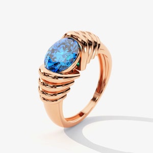 May include: A rose gold ring with a large blue gemstone set in a twisted band.