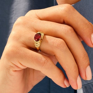 May include: A gold ring with a red gemstone set in a textured band.