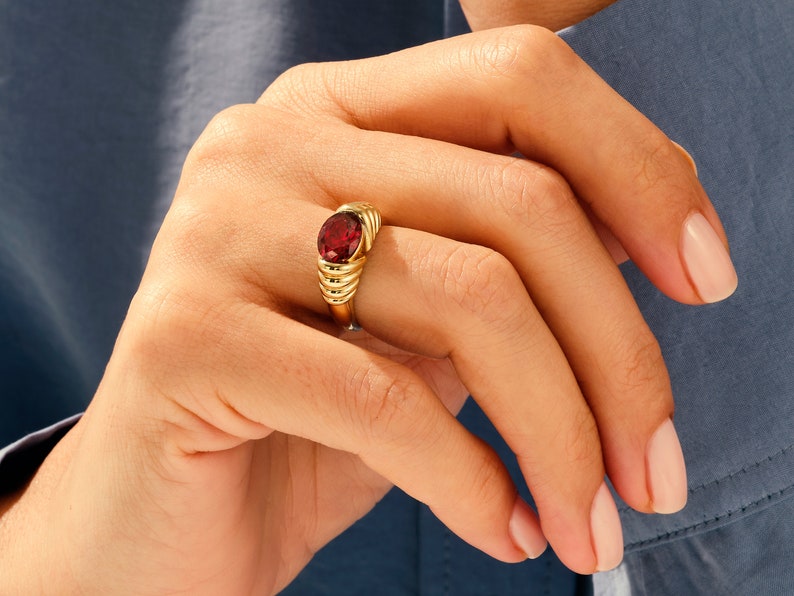 May include: A gold ring with a red gemstone set in a textured band.