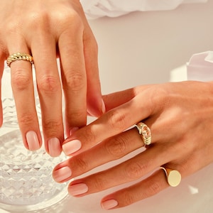 May include: Close-up of two hands wearing gold rings. The rings are a thick, twisted band and a ring with a clear stone set in a gold band. The hands are resting on a glass of water.