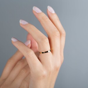 May include: A simple gold band ring on a person's finger.