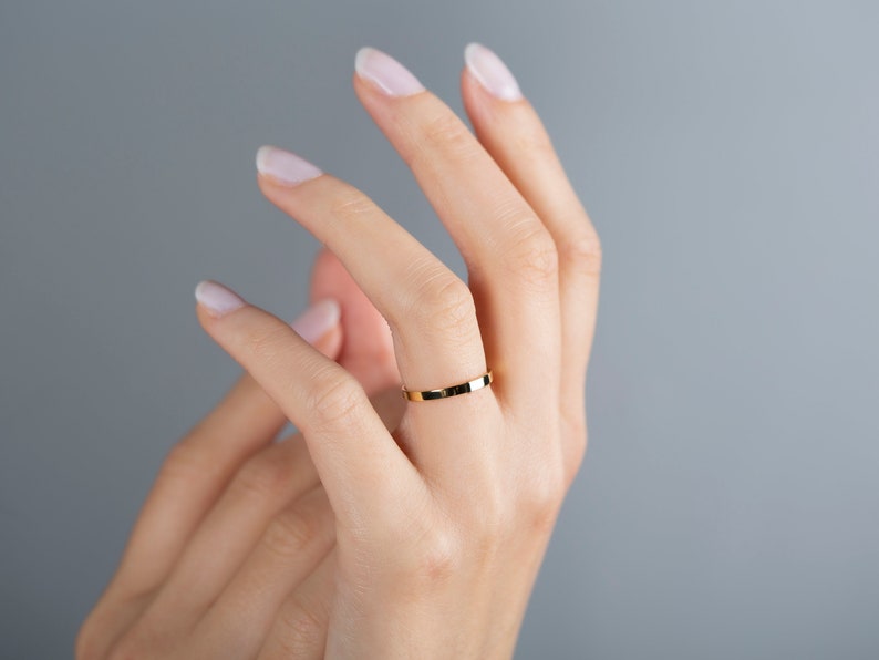 May include: A simple gold band ring on a person's finger.