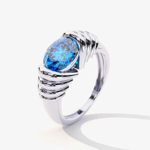 May include: A silver ring with a large, oval-shaped blue gemstone set in the center. The band of the ring is intricately designed with multiple layers of metal.