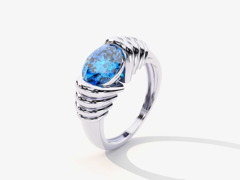 May include: A silver ring with a large, oval-shaped blue gemstone set in the center. The band of the ring is intricately designed with multiple layers of metal.