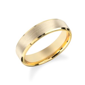 Può includere: Un anello in oro con una fascia larga caratterizzata da una finitura spazzolata e opaca sulla superficie esterna e bordi lucidi e brillanti. L'interno della fascia è liscio e riflettente, con una tonalità oro giallo brillante.
