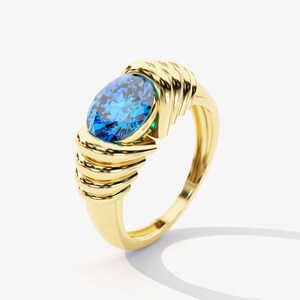 May include: A gold ring with a large blue oval-shaped gemstone set in the center. The ring band is intricately designed with multiple gold bands.