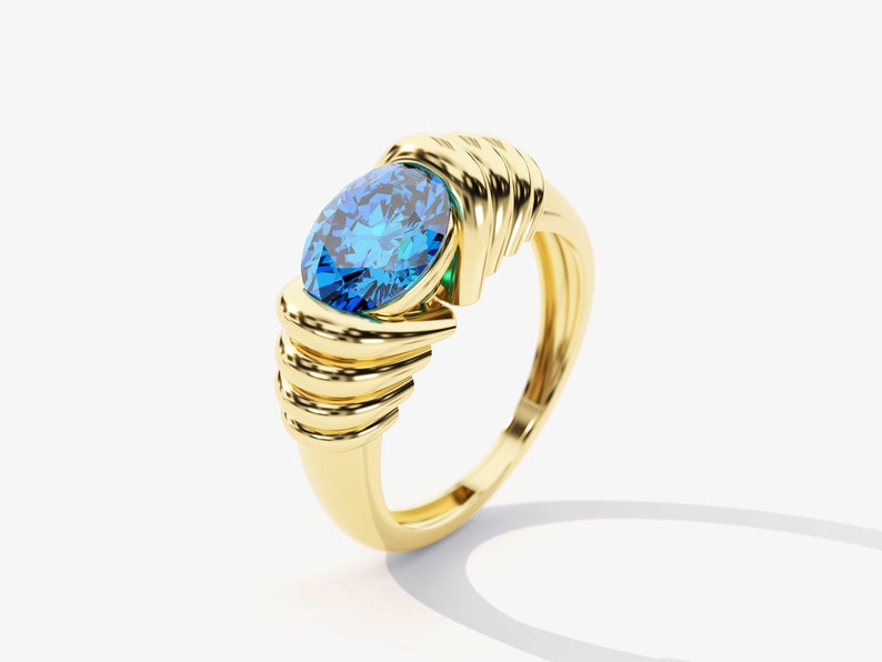 May include: A gold ring with a large blue oval-shaped gemstone set in the center. The ring band is intricately designed with multiple gold bands.