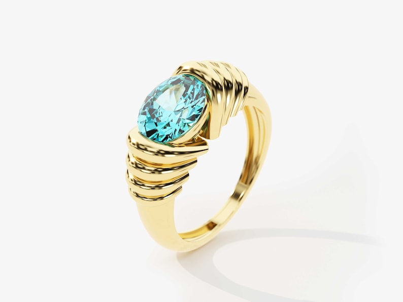 May include: A gold ring with a large, oval-shaped, light blue gemstone set in the center. The band of the ring is intricately designed with multiple layers of gold.