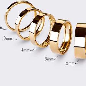 May include: A selection of gold wedding rings, ranging in width from 2mm to 6mm. The rings are presented on a light background, highlighting their polished surfaces. Sizes are indicated in millimetres.