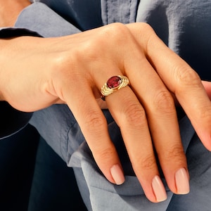 May include: A gold ring with a red gemstone set in a twisted band.