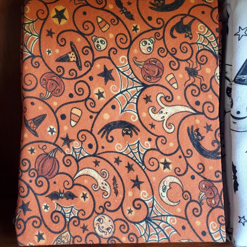 May include: Orange fabric with a black and white Halloween pattern. The pattern includes bats, spiders, pumpkins, ghosts, and stars.