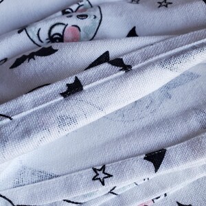 May include: White fabric with a black and white pattern of bats, stars, and moons. The fabric is folded over, showing the stitching on the edges.