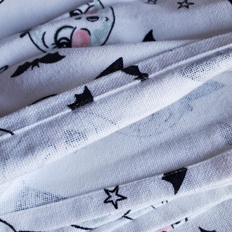 May include: White fabric with a black and white pattern of bats, stars, and moons. The fabric is folded over, showing the stitching on the edges.