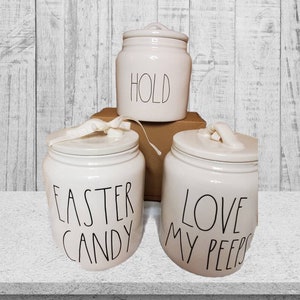 Puede incluir: Tres botes de cer&aacute;mica blanca con letras negras. Los botes est&aacute;n etiquetados con "Hold", "Easter Candy" y "Love My Peeps".