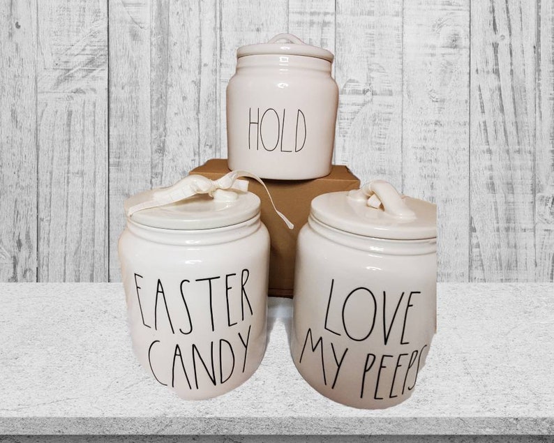 Puede incluir: Tres botes de cer&aacute;mica blanca con letras negras. Los botes est&aacute;n etiquetados con "Hold", "Easter Candy" y "Love My Peeps".