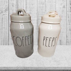 Puede incluir: Dos botes de cer&aacute;mica con tapas, uno gris con la palabra "COFFEE" y otro blanco con la palabra "PEEPS".