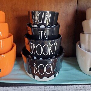 May include: A set of four black ceramic nesting bowls with white dripping paint and Halloween-themed words. The bowls are stacked from largest to smallest, reading "BOO!" "SPOOKY", "EEK!" and "SCARY".