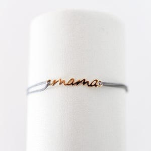May include: A delicate grey string bracelet with a gold charm that says "mama".