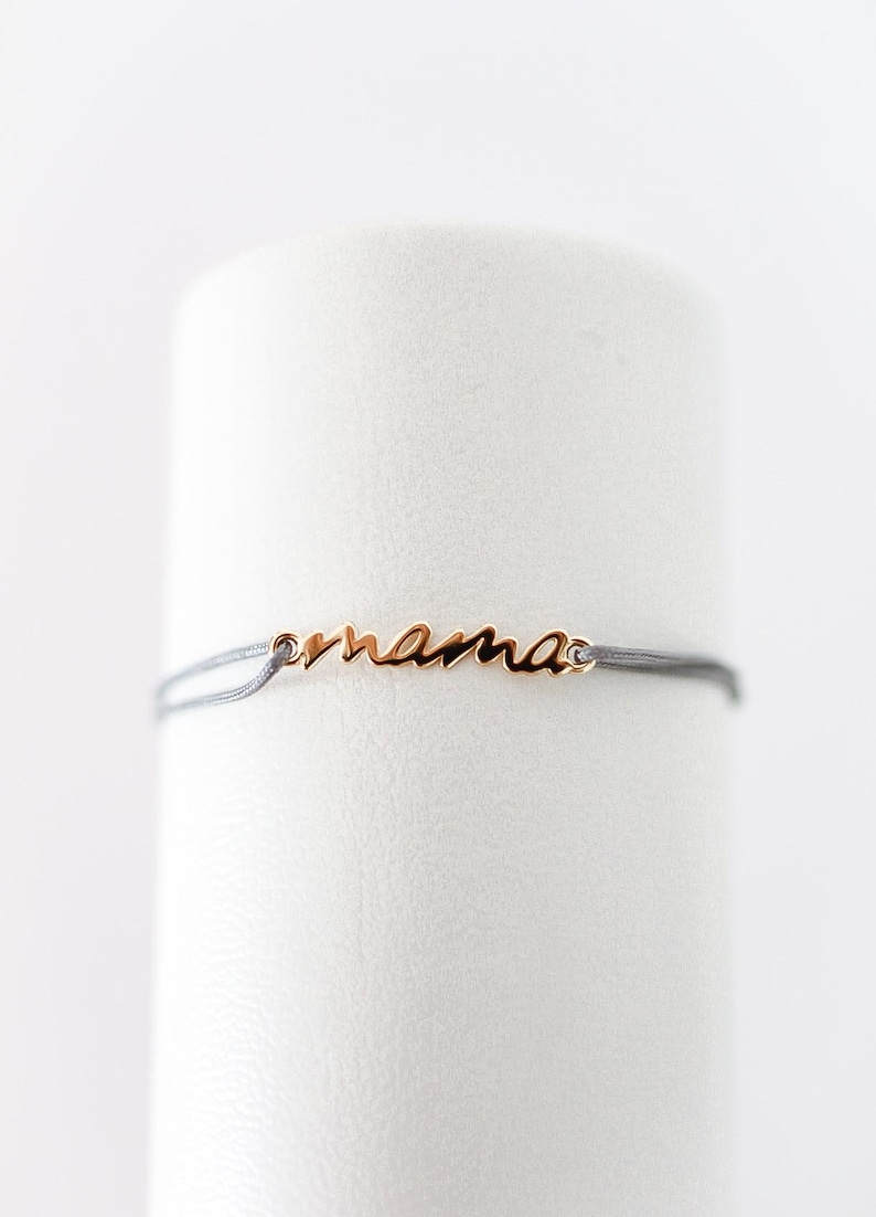 May include: A delicate grey string bracelet with a gold charm that says "mama".