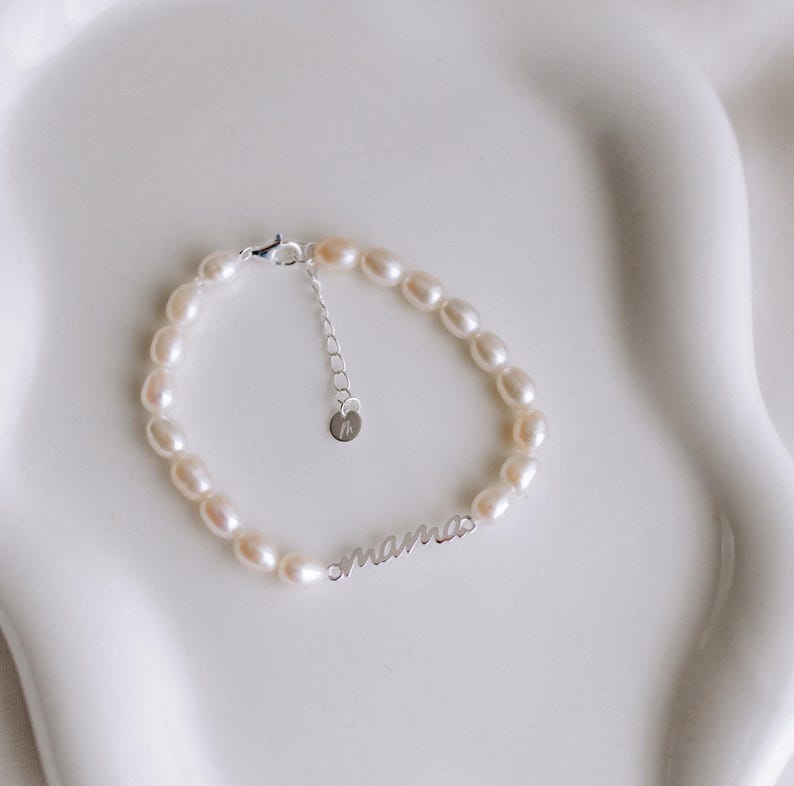 May include: A delicate pearl bracelet with a silver charm that reads "mama".