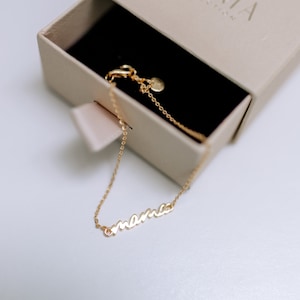 May include: A gold chain bracelet with the word "mama" spelled out in cursive.