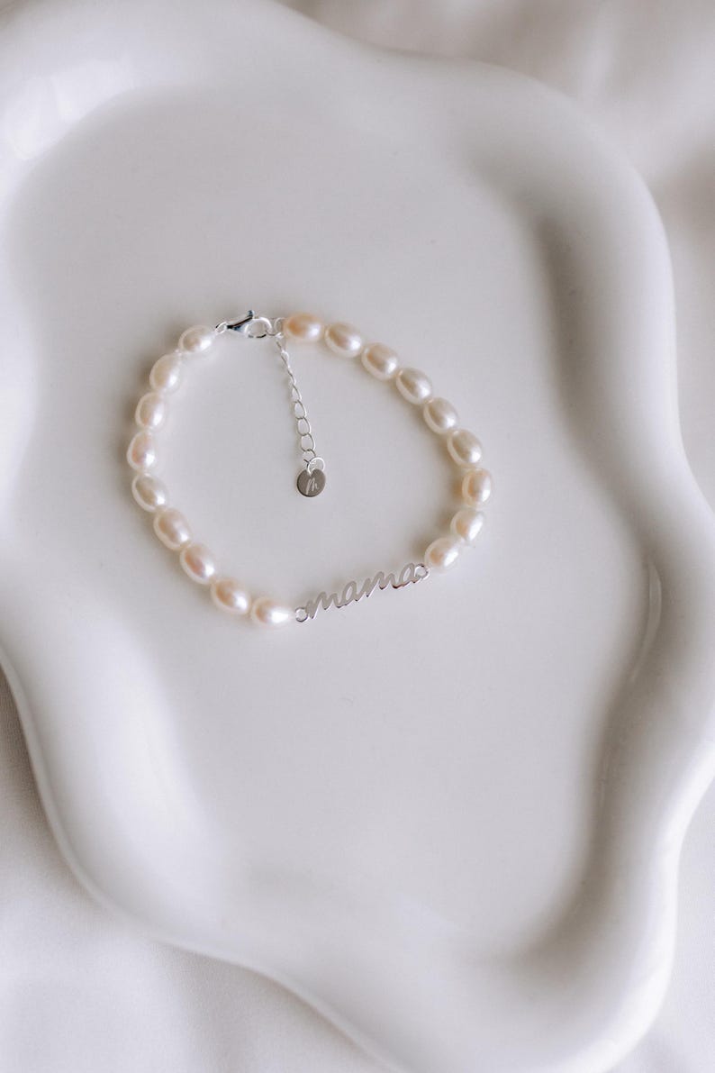 May include: A delicate pearl bracelet with a silver charm that reads "mama".