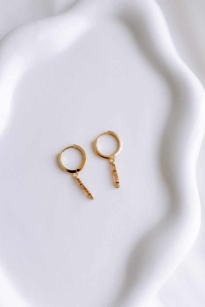May include: A pair of gold hoop earrings with a dangling chain of small gold beads.
