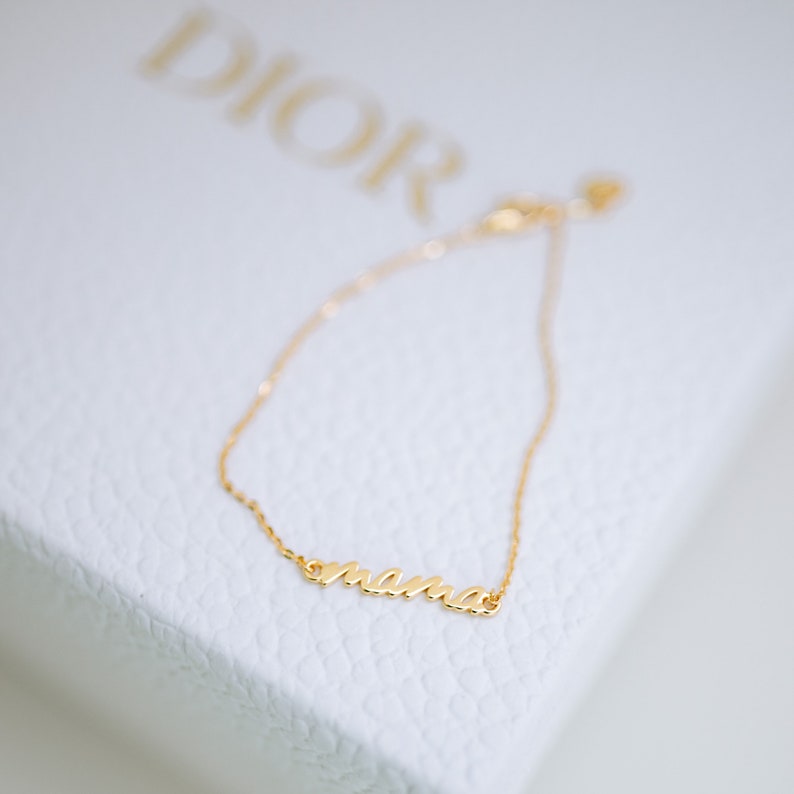 May include: A gold chain bracelet with the word "mama" spelled out in cursive.