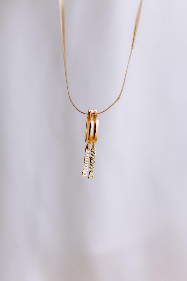 May include: Gold hoop earrings with a dangling charm that says "mama" in cursive.