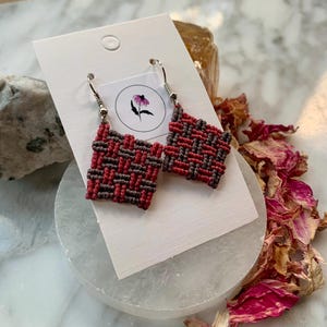 May include: A pair of woven earrings with a square shape. The earrings are made with red and brown thread and have silver hooks.