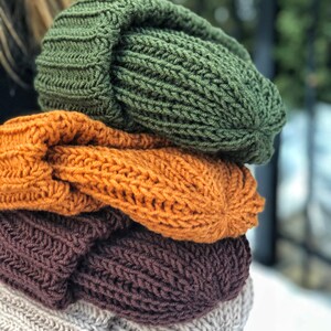 Puede incluir: Una pila de cuatro gorros de punto en diferentes colores: verde, naranja, marr&oacute;n y beige. Los gorros est&aacute;n doblados y apilados uno encima del otro.