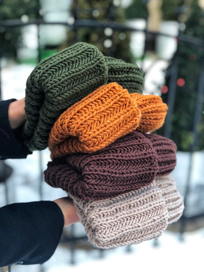 Puede incluir: Cuatro gorros de punto apilados uno encima del otro. Los gorros son de diferentes colores: verde, naranja, marr&oacute;n y beige.