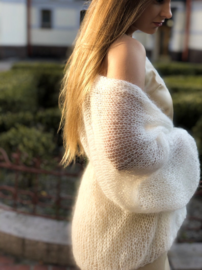 May include: A white, lightweight knit cardigan with a delicate open-weave pattern. The cardigan has long sleeves and a relaxed fit.