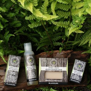 May include: A set of three natural insect repellent products: a repair balm, a body oil, and a bar of soap. All products are labeled "Herbal Insect" and feature a green plant logo. The products are displayed on a wooden log with a fern background.
