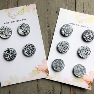 May include: Two sets of six round, black and white ceramic tiles with different patterns. The tiles are arranged in rows of three on white cards with the text "ARS STUDIO 74".