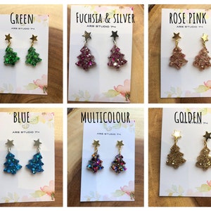 Peut inclure: Six paires de boucles d'oreilles en forme de sapin de Noël sur des cartes blanches avec les mots "Vert", "Fuchsia & Argent", "Rose Poudré", "Bleu", "Multicolore" et "Doré" imprimés dessus. Chaque paire de boucles d'oreilles est ornée d'un petit charme étoile dorée au sommet de l'arbre.