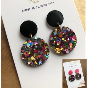 Op de afbeelding: Een paar oorhangers met zwarte en veelkleurige glitter ronde schijven. De oorbellen zijn op een witte kaart met de tekst "ARS STUDIO 74".